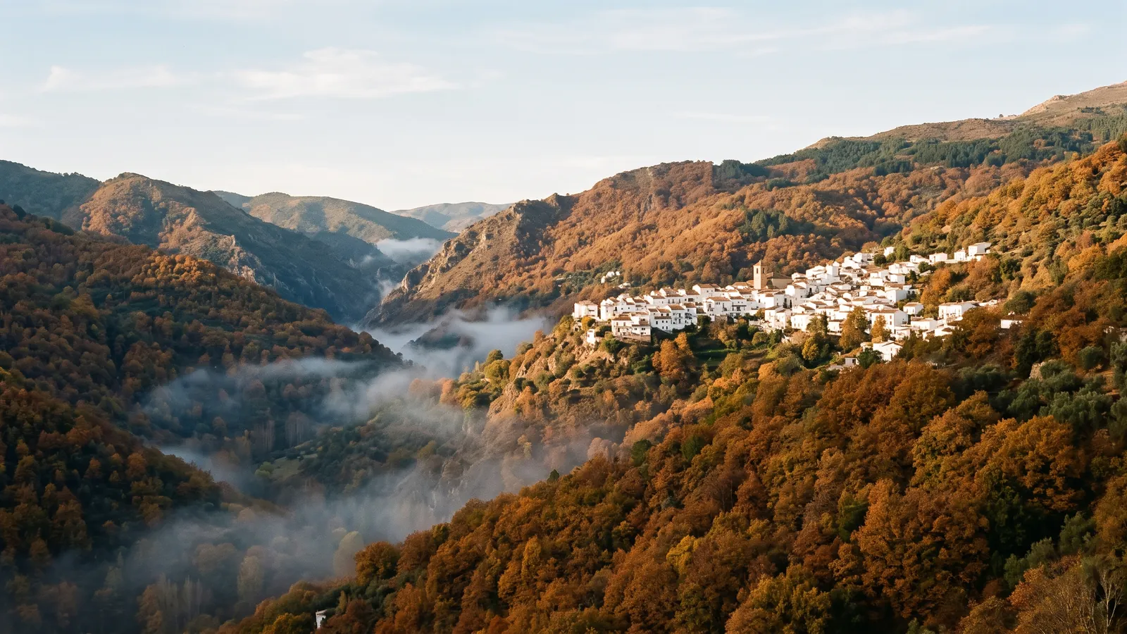 Bergtal im Herbst mit kupferfarbenen Kastanienwäldern und einem weißen Dorf am Hang