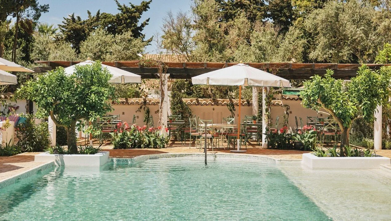 Pool mit Brunnen und schattigen Tischen zwischen Olivenbäumen auf der Finca Ana María des Marbella Club