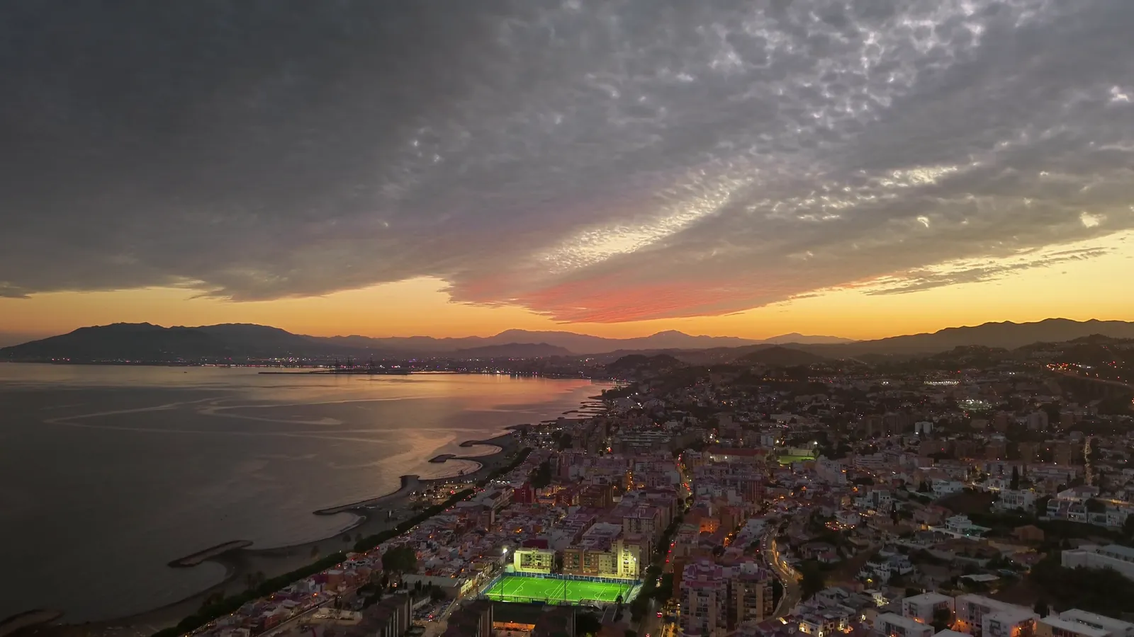Luftaufnahme der Küste von Málaga bei Sonnenuntergang mit den Lichtern der Stadt und Bergen im Hintergrund